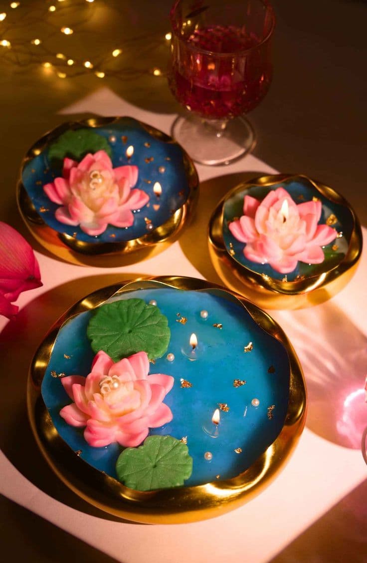 Three lit pink lotus candles in gold bowls with blue wax and green lily pads.